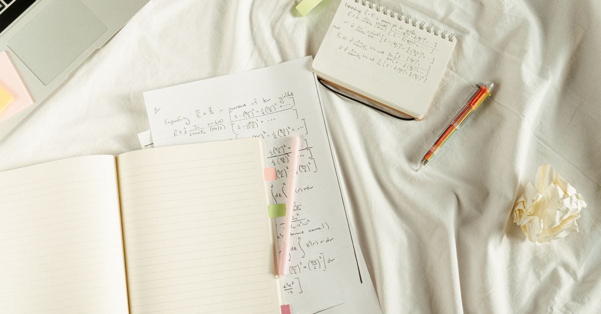 Flat lay of a cozy study space with notebooks, math formulas, and laptop on bed.