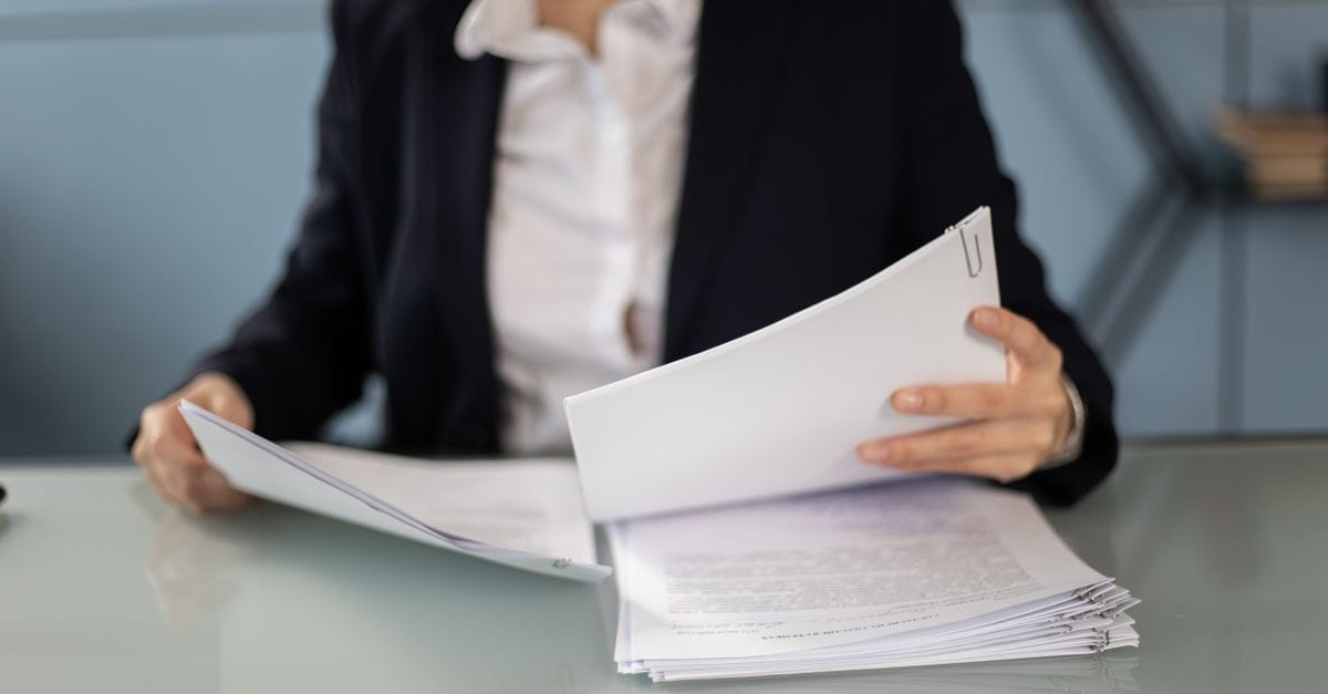 Businesswoman in formal attire reviewing and organizing documents at an office desk.