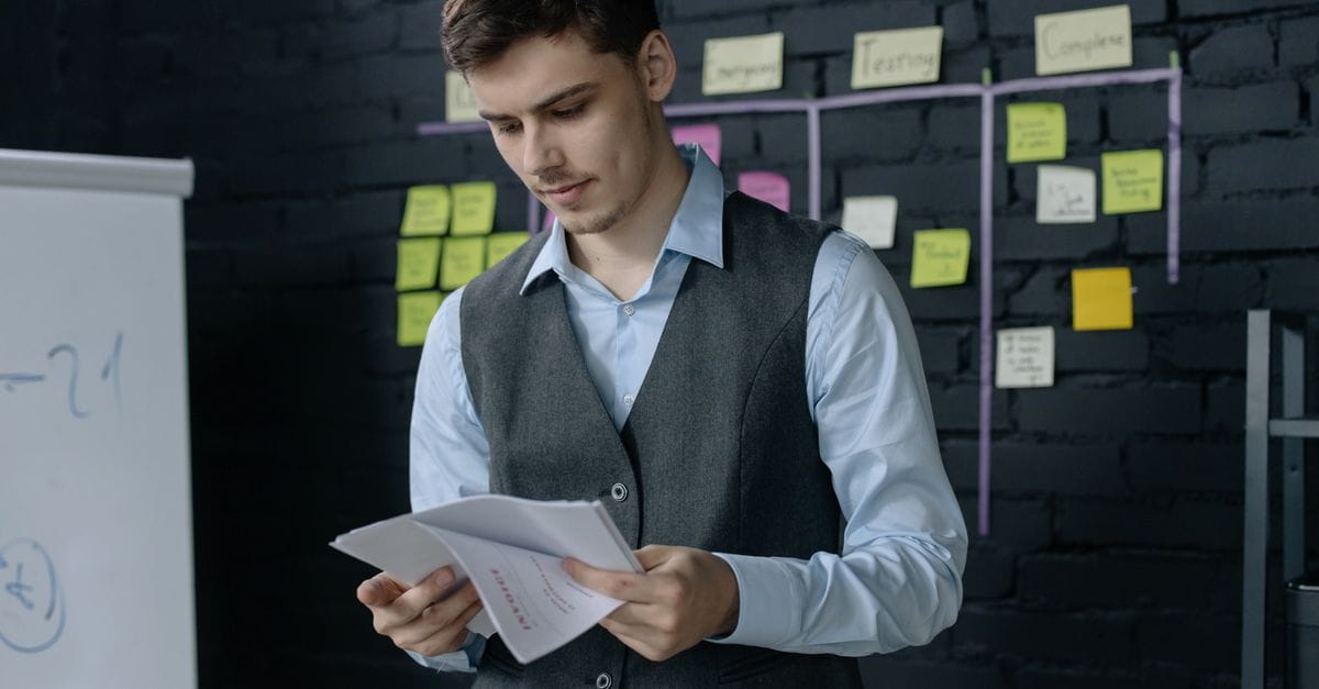 A young man reviewing documents in an office with a black brick wall and sticky notes background.