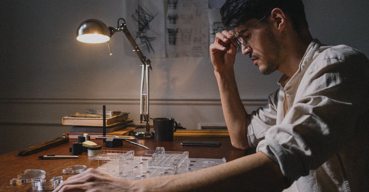 Architect seated at a desk, working on a model under a desk lamp, focusing intently.