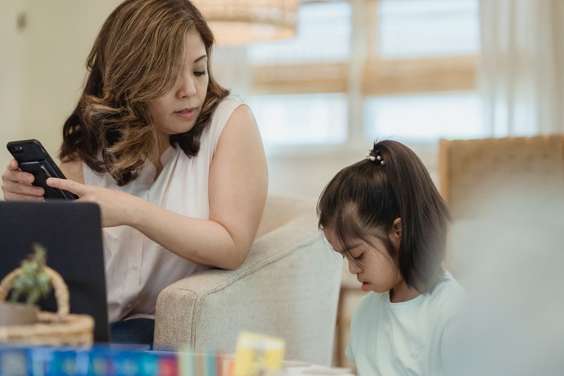 A mother using a smartphone while her daughter reads nearby, creating a warm family moment.