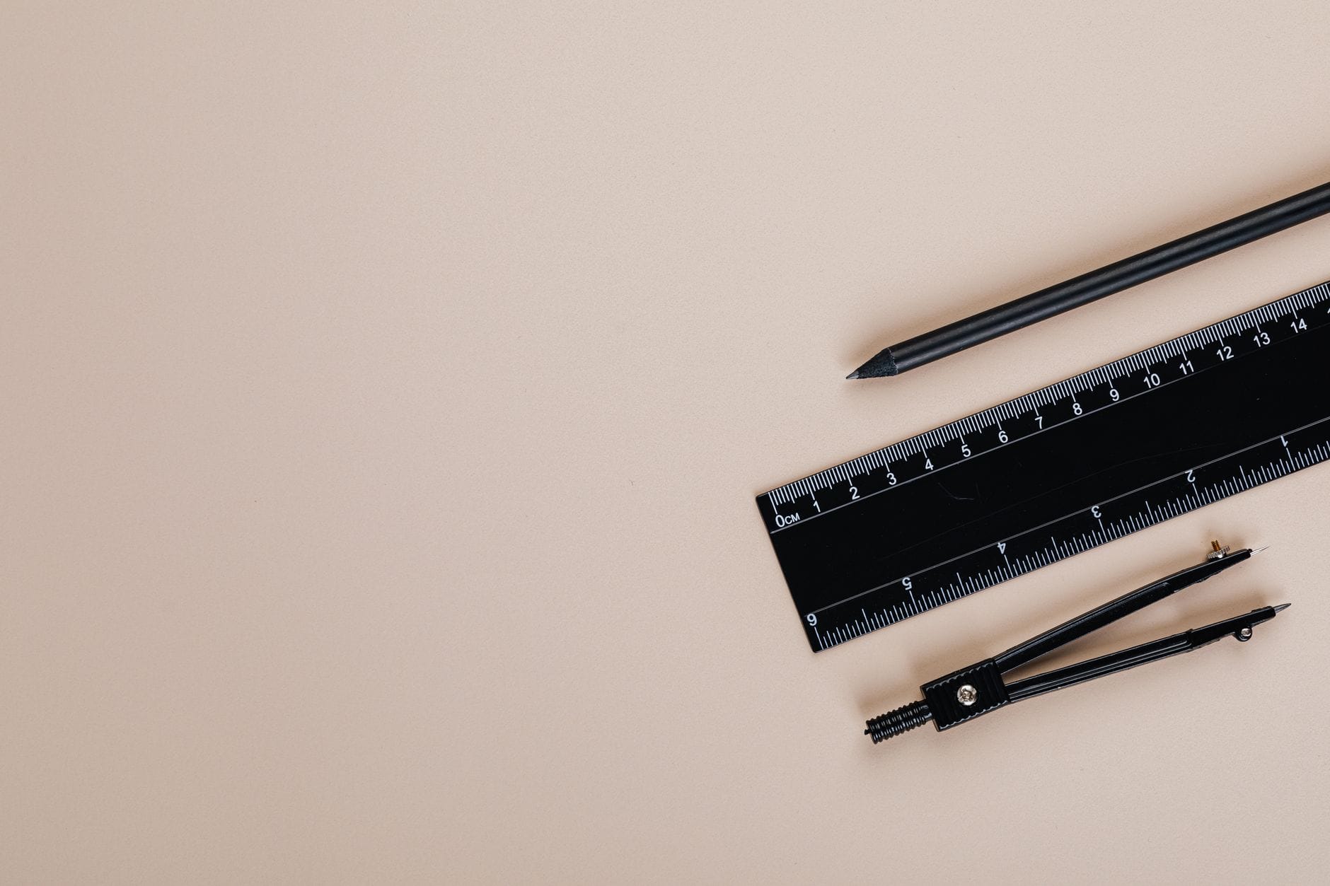 Minimalist flat lay of a compass, pencil, and ruler on a cream-colored background.