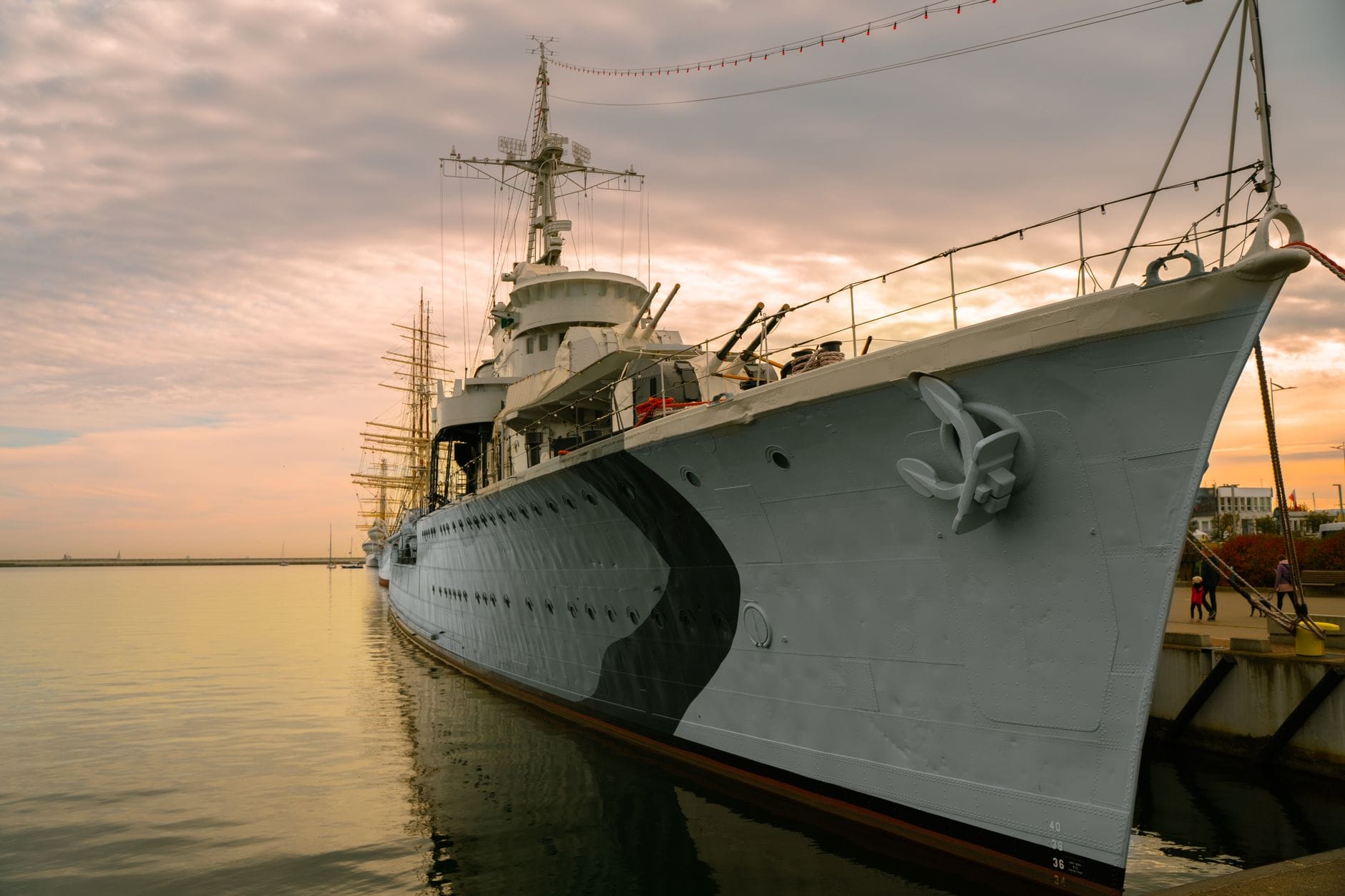 A large warship anchored at a peaceful harbor during sunset, reflecting on serene water.