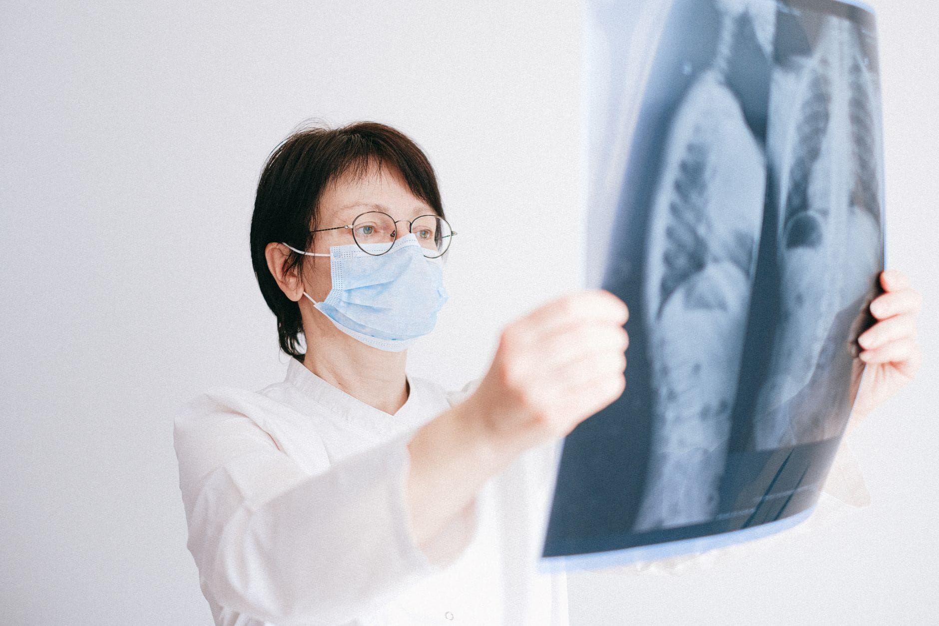Doctor analyzes lung x-ray wearing a mask in a clinical setting.