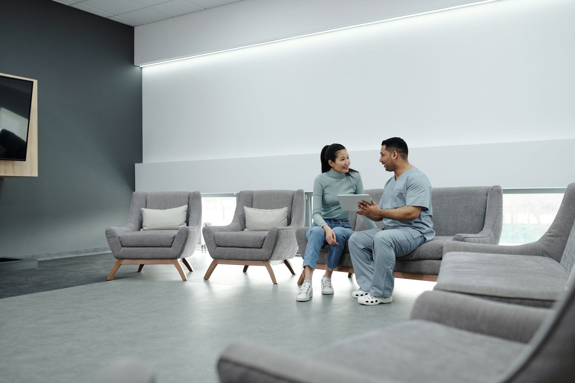 Doctor and patient discussing health in a modern waiting room with digital tablet.