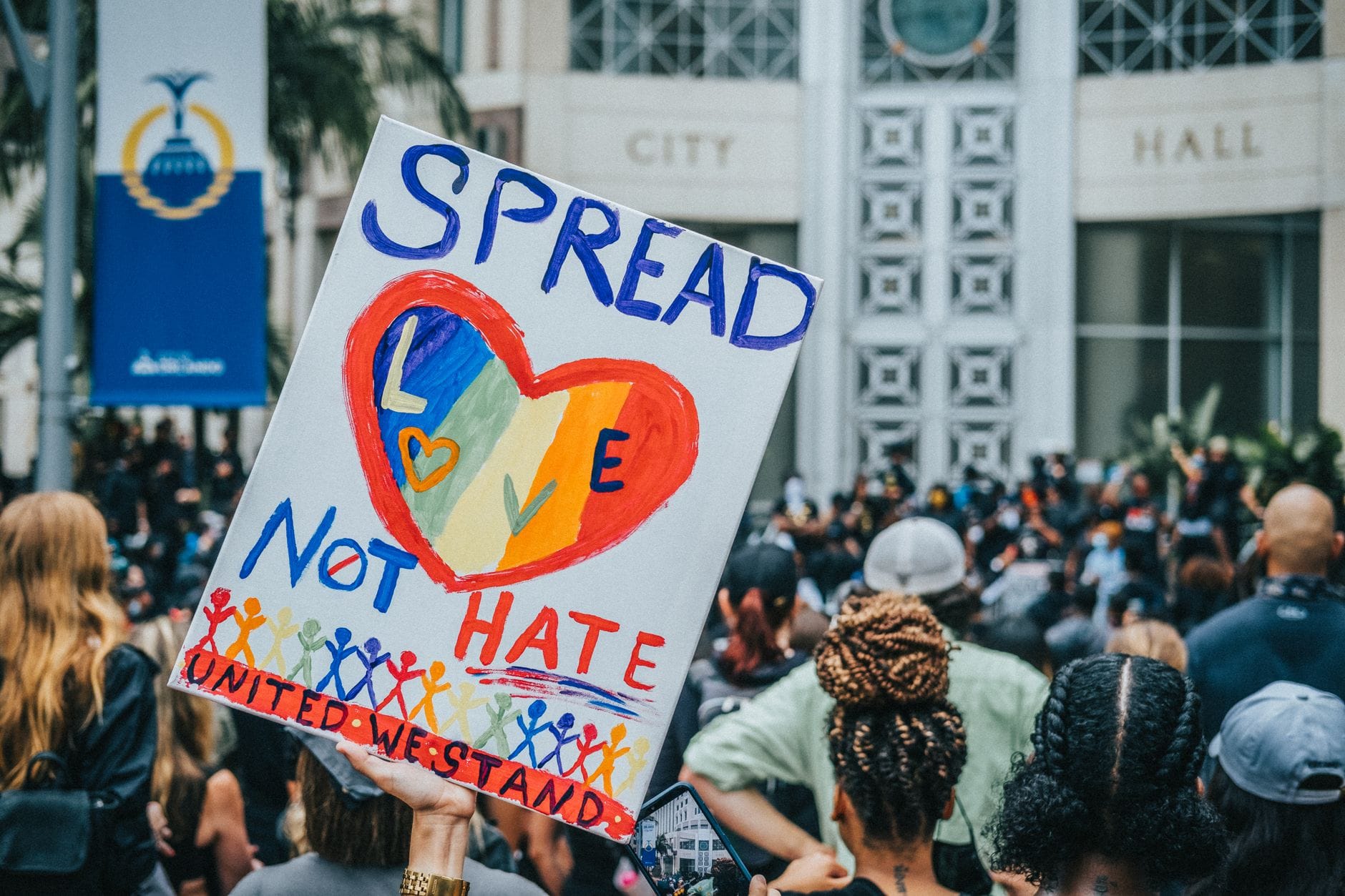 A colorful protest sign promoting love over hate during a rally at City Hall, capturing a peaceful advocacy movement.