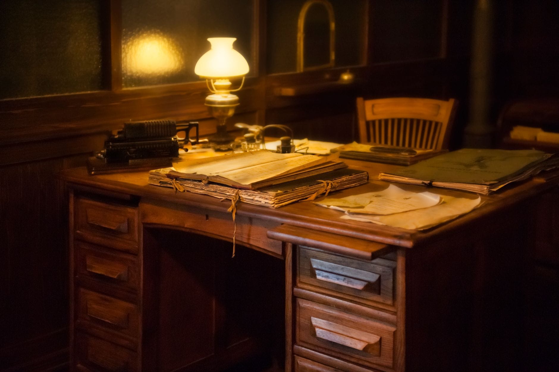 Cozy vintage office setting with an antique typewriter, lamp, and paperwork on a wooden desk.